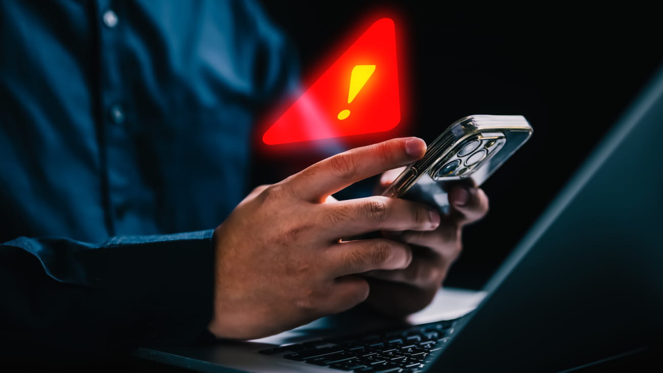 A person holding a smartphone with a warning triangle above