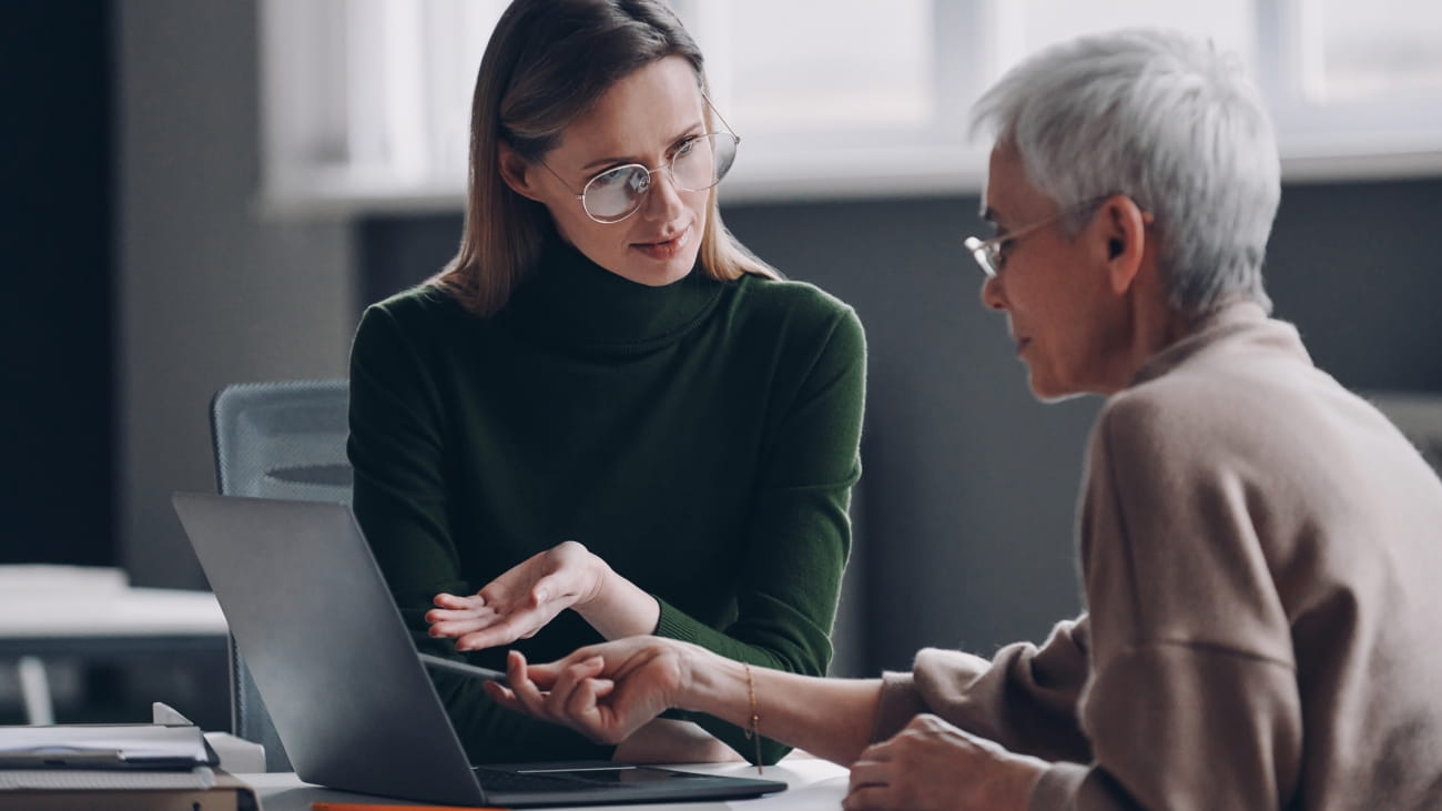 Confident financial advisor pointing laptop while discussing options with senior woman in office