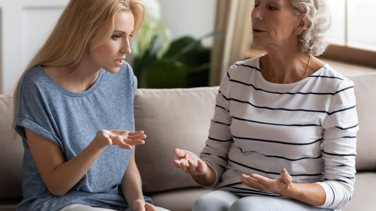 Stressed young blonde grown up daughter arguing with nervous old mature mother, sitting together at home. Irritated elderly woman lecturing adult child, different generations misunderstanding gap.