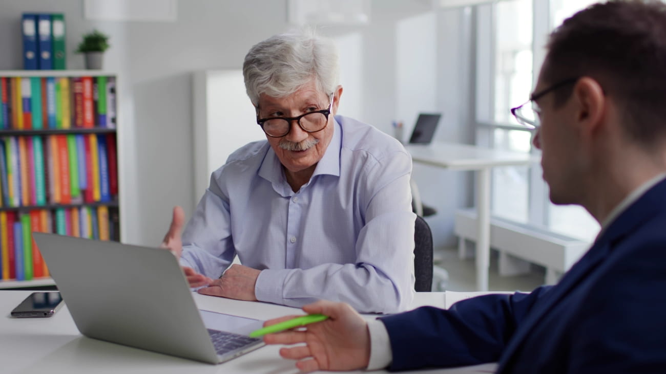 Sales manager advise aged client showing education program on laptop. Senior man having appointment with broker talking about savings investment.
