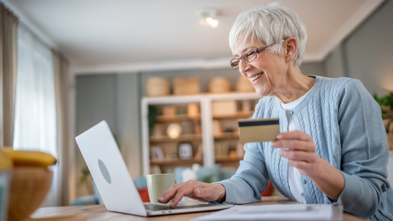 One mature senior woman grandmother sit at home use credit or debit card for online shopping browse internet stores buying stuff on discount sale real people copy space use laptop computer