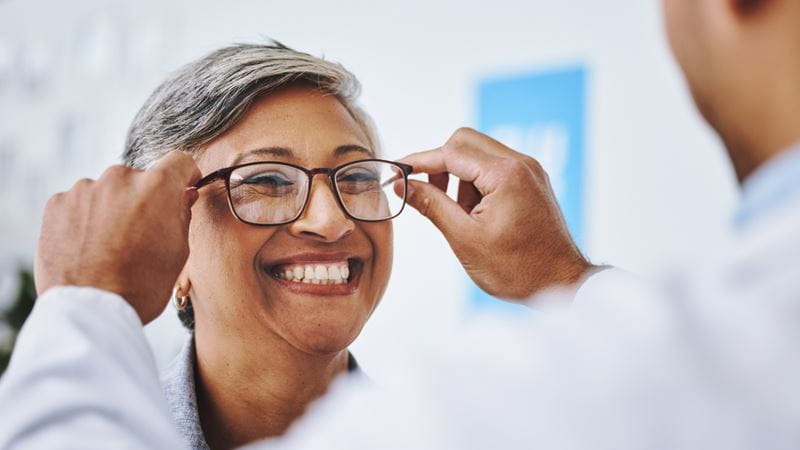 Optometry, smile and woman with prescription glasses, optician and helping client with product. Female person, employee and optometrist assist with eyewear, clear vision and buying new spectacles