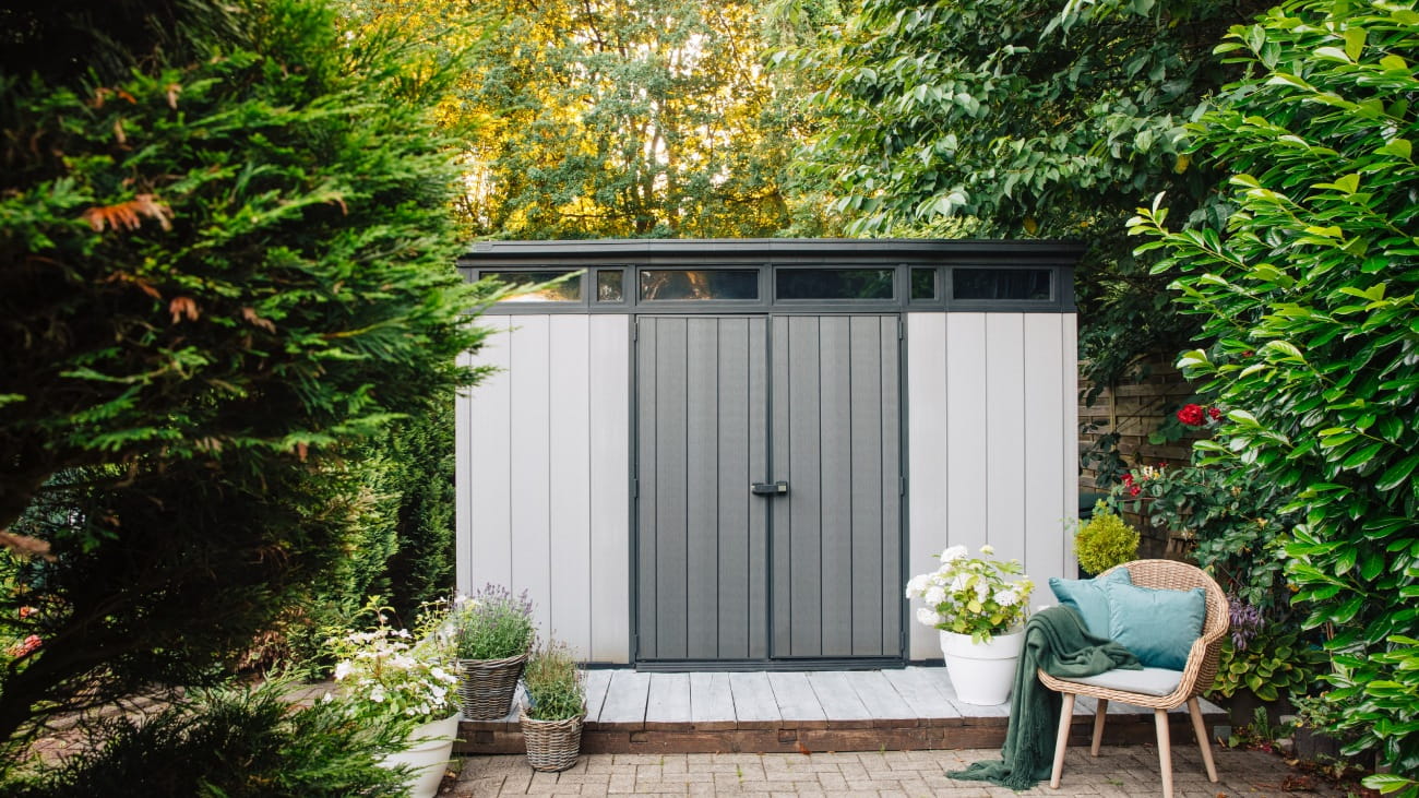 Gray garden shed in summer. Lots of pots of flowers next to a plastic garden shed. Relax in the garden. Big garden in Germany 