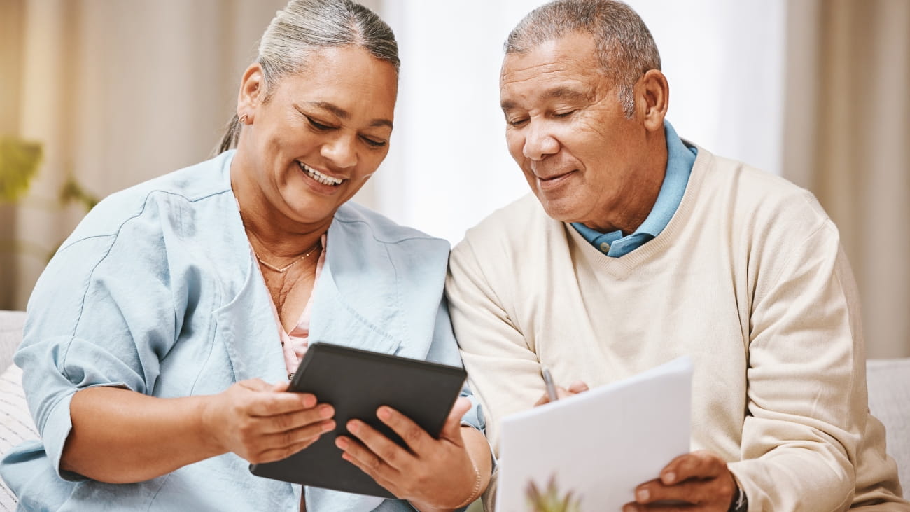 Smiling Senior Couple Sitting Around Table At Home Reviewing Finances Using Digital Tablet.