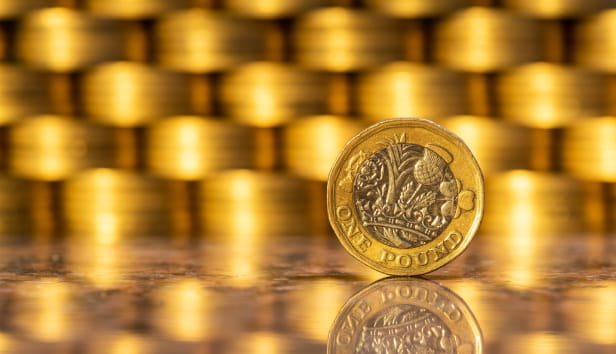 A British pound coin with many gold coins in the background.