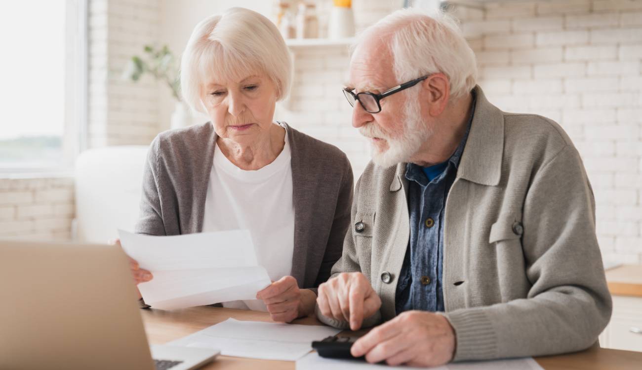 enior couple grandparents family counting funds on calculator, doing paperwork, at home using a laptop