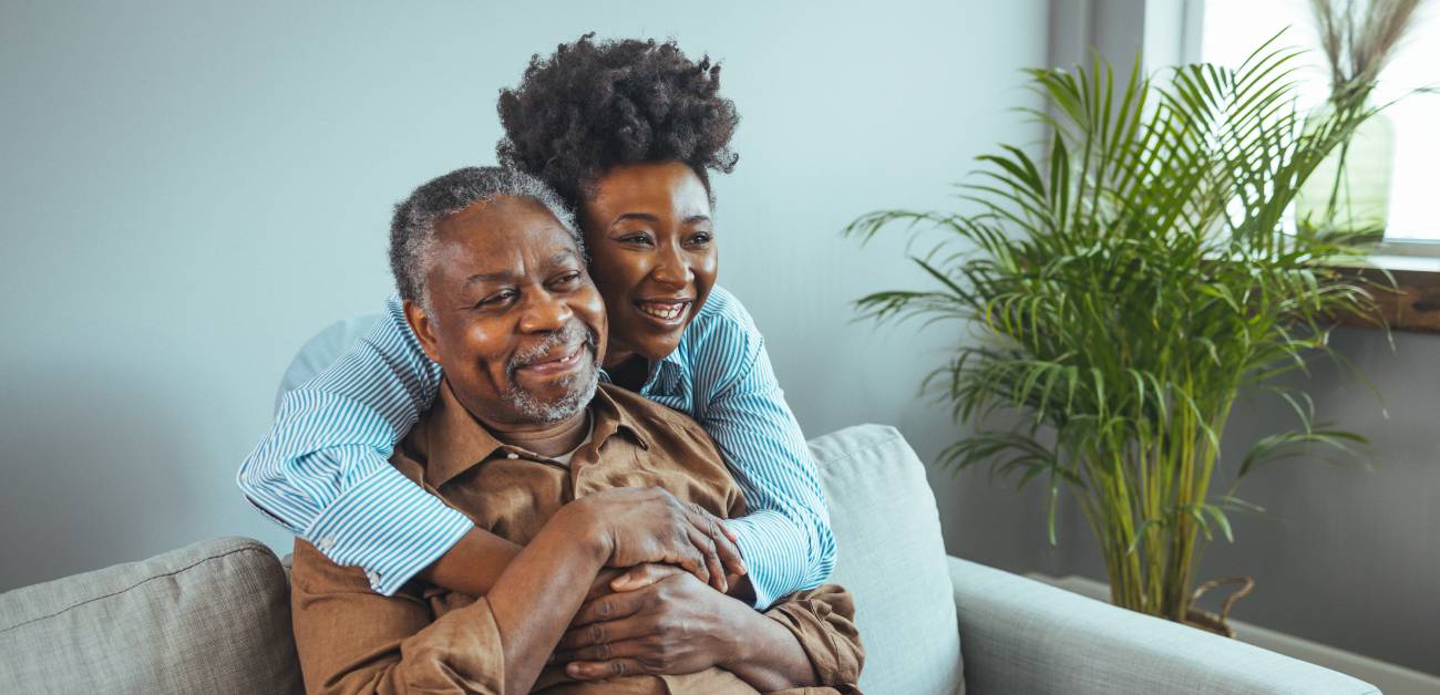 A woman hugging her elderly father as he sits in the sofa