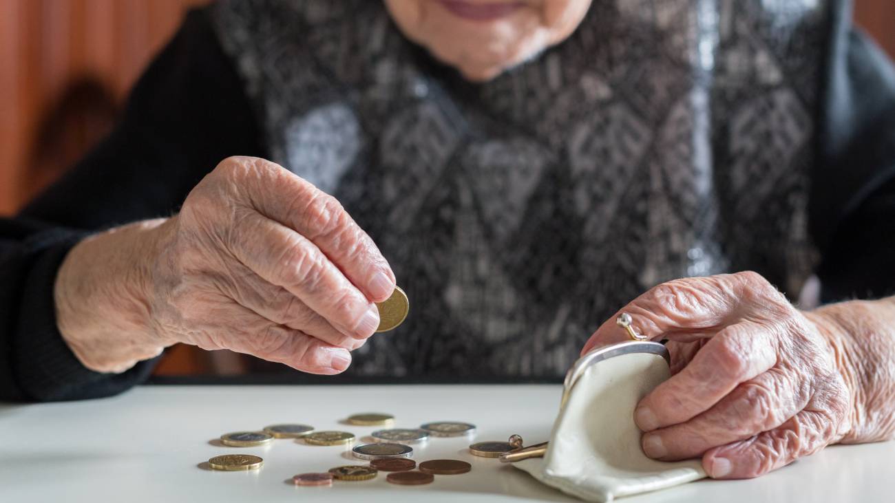 The hands of an elderly woman sitting at a table counting the coins in her purse