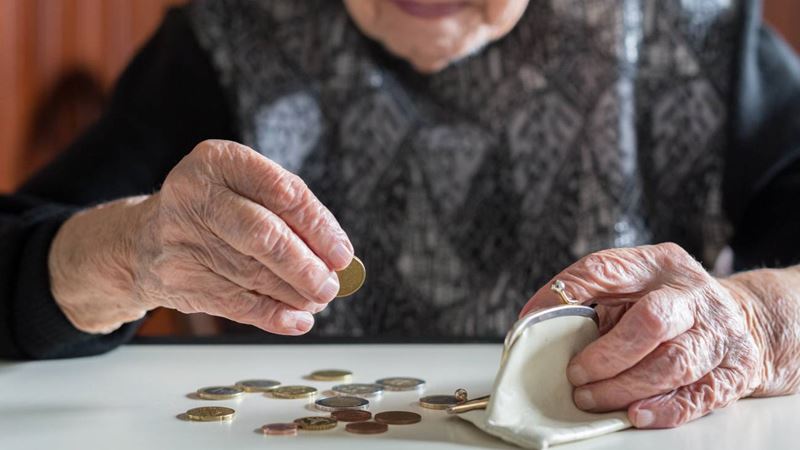 The hands of an elderly woman sitting at a table counting the coins in her purse