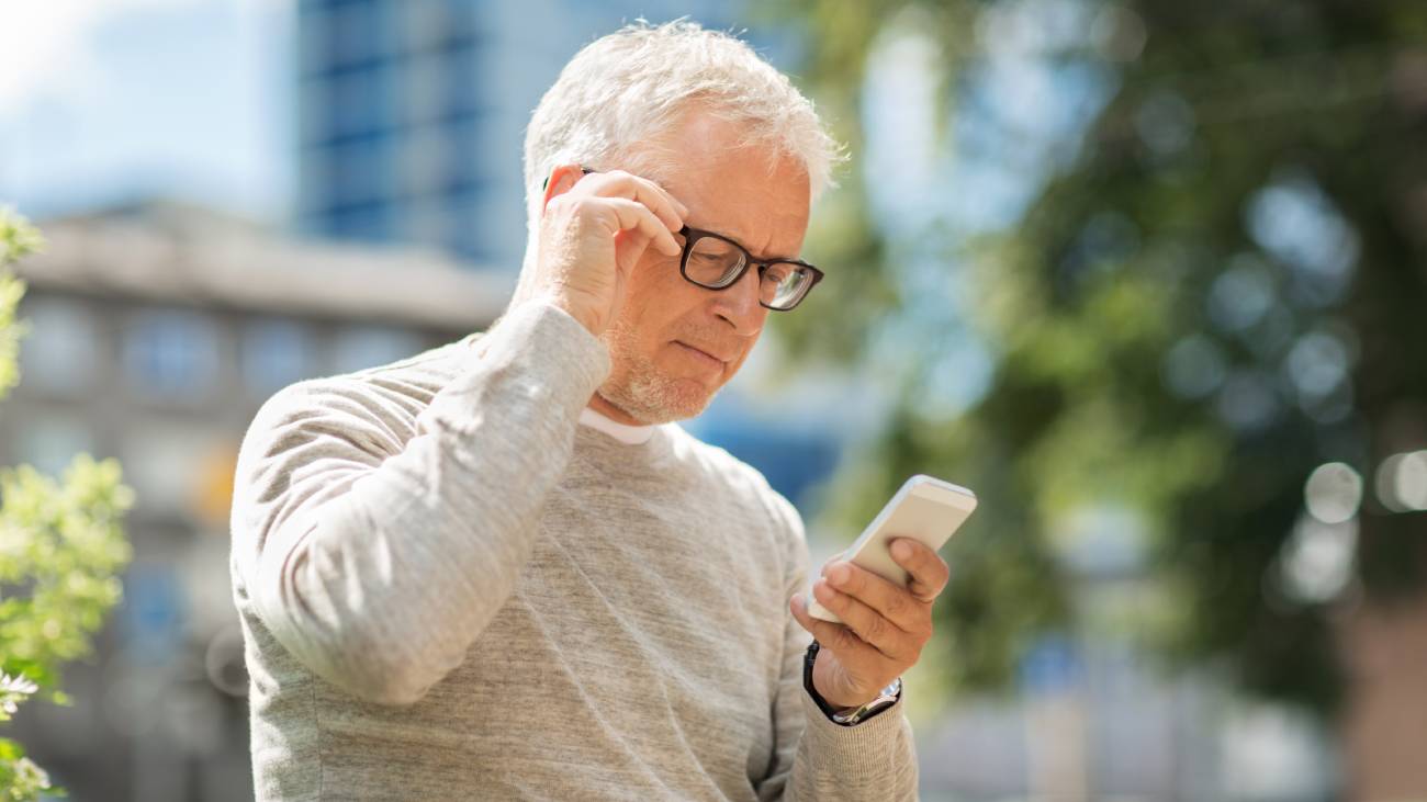 A mature male, holding his glasses while looking at his phone