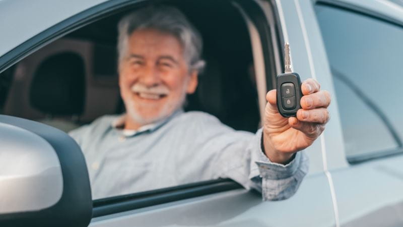 Portrait of happy senior man showing keys of car to the camera of a new car purchase.