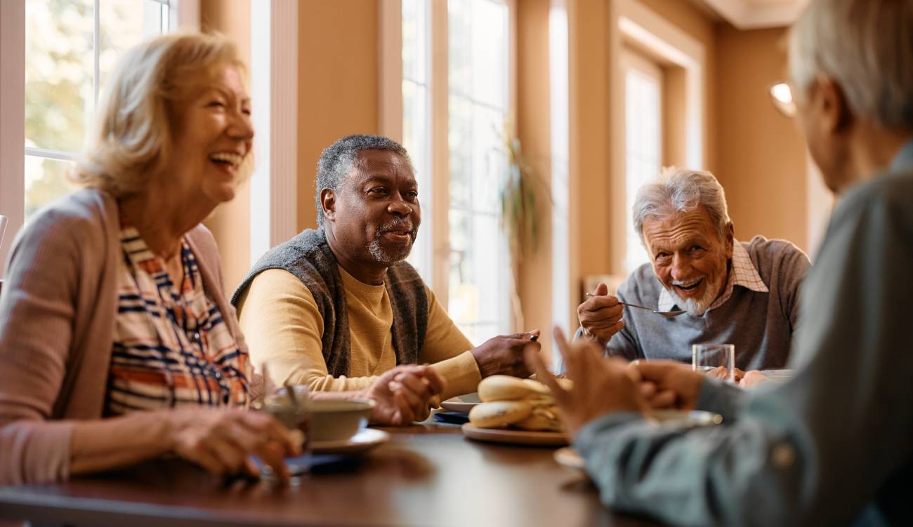 Happy senior man talking to his friends while eating at dining table at nursing home.