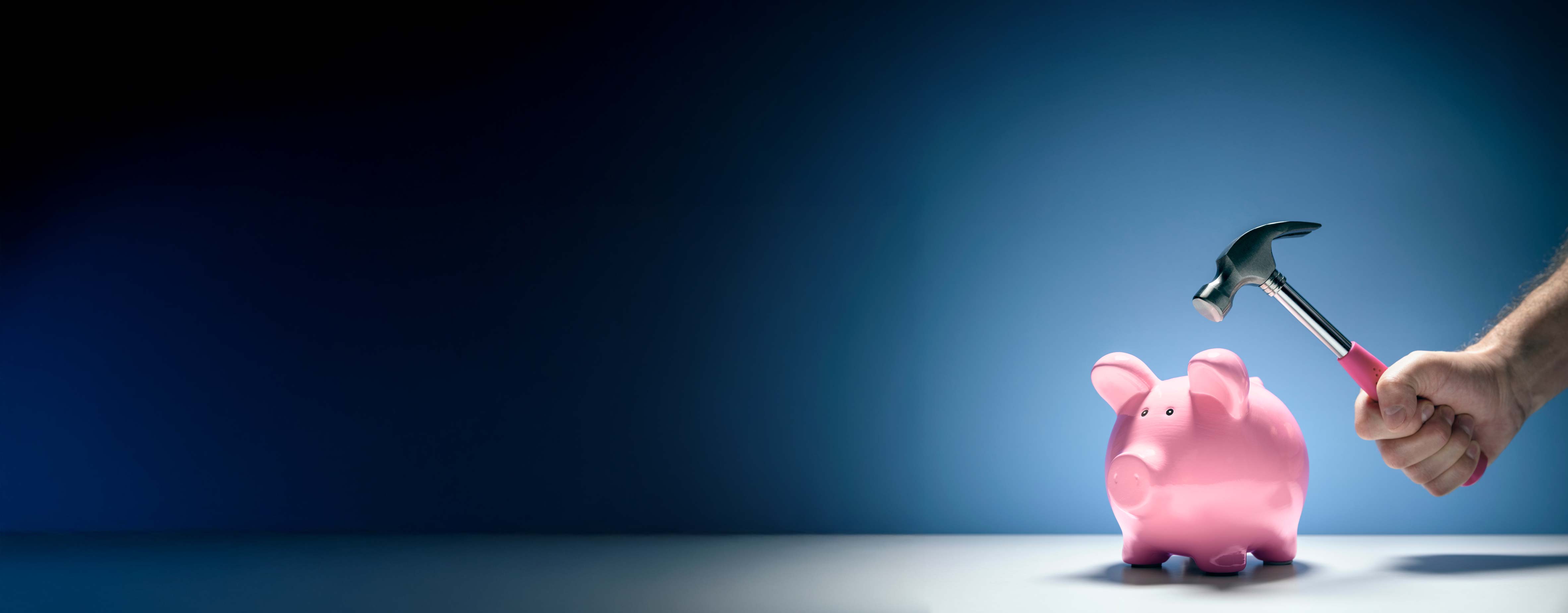 A piggybank with a hammer being held above it