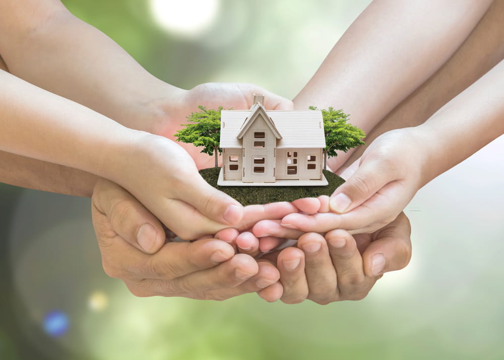 Four pairs of hands holding a wooden toy house