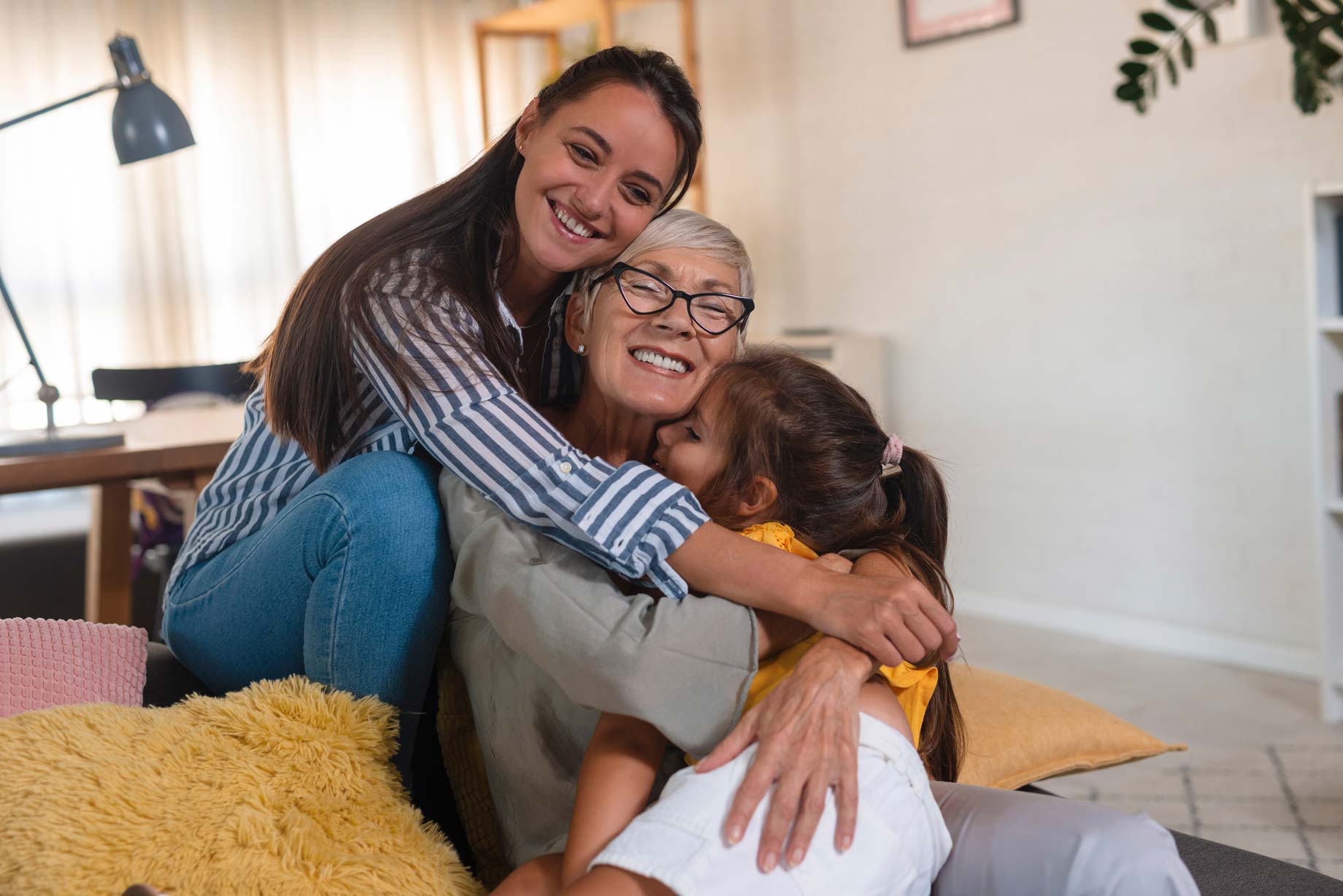 A grandmother being cuddled by her daughter and granddaughter at home on the sofa
