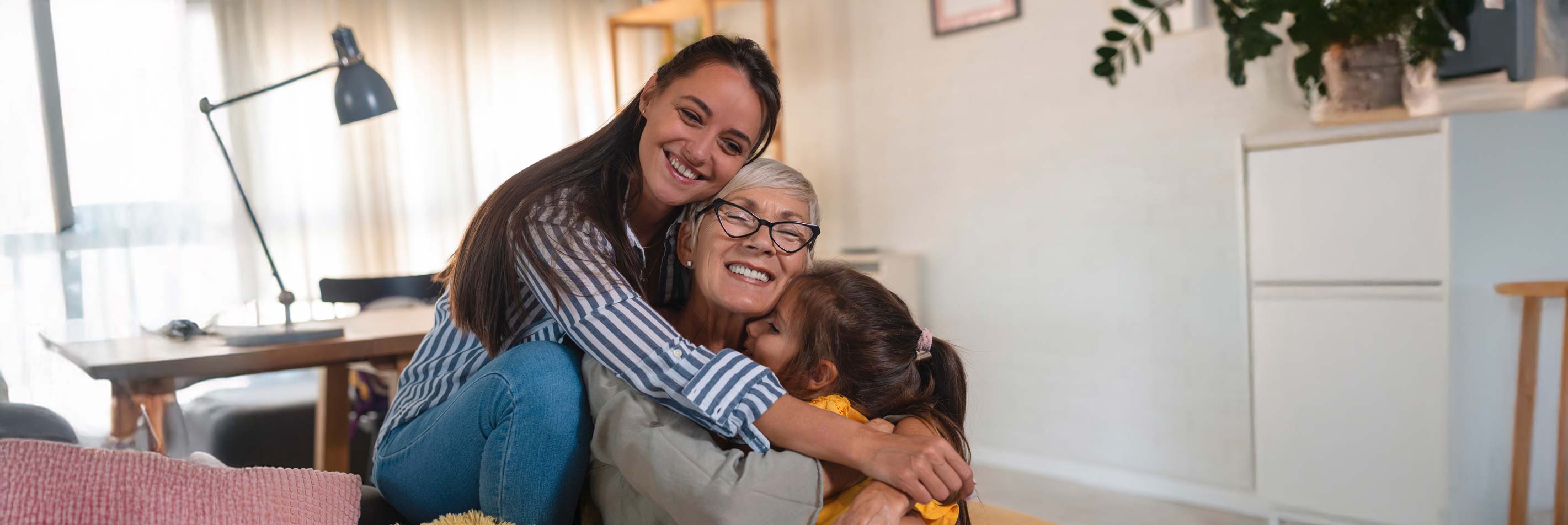 A grandmother being cuddled by her daughter and granddaughter at home on the sofa