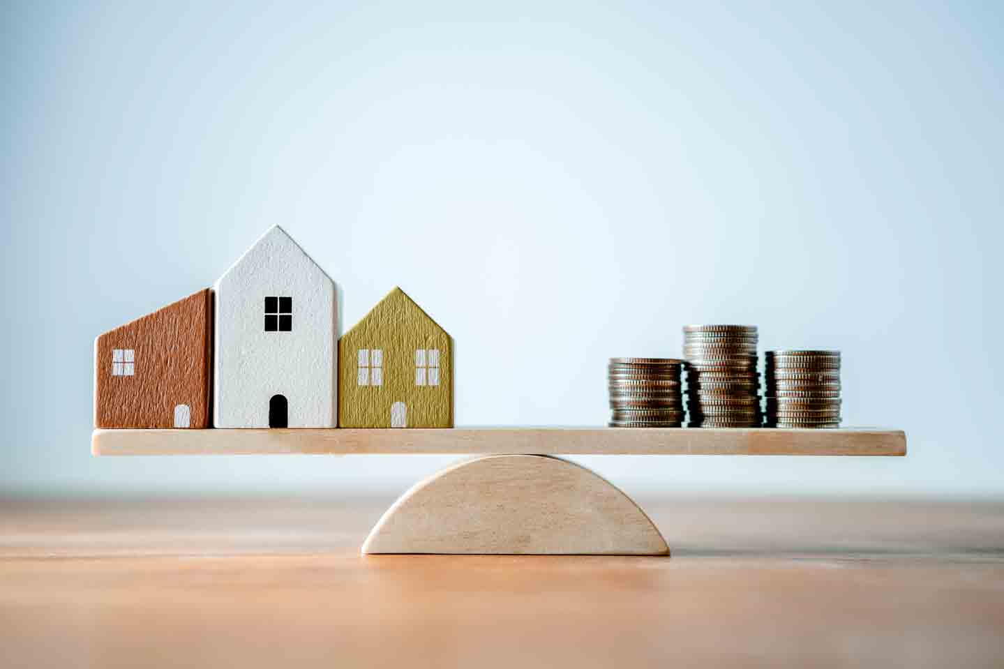 small wooden houses and 3 piles of coins on opposite ends of a seesaw