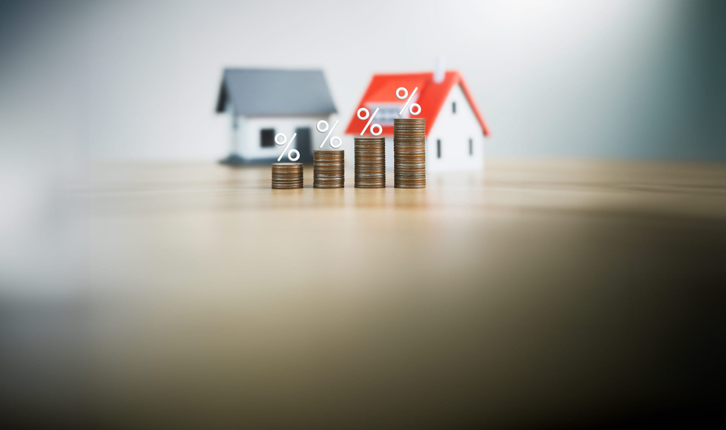 Two wooden houses with increasingly tall piles of coins with percentage symbols above them