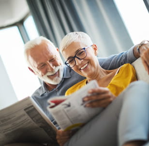 Two smiling older people sitting on a sofa looking the Saga Equity Release guide