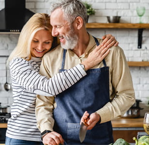 Two older people smiling and hugging in a kitchen