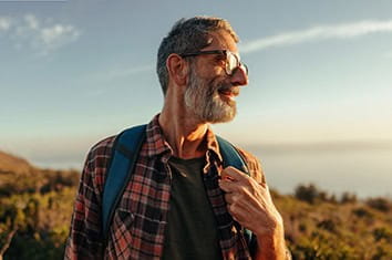 Happy mature hiker with a smile on his face while standing on top of a hill with a backpack