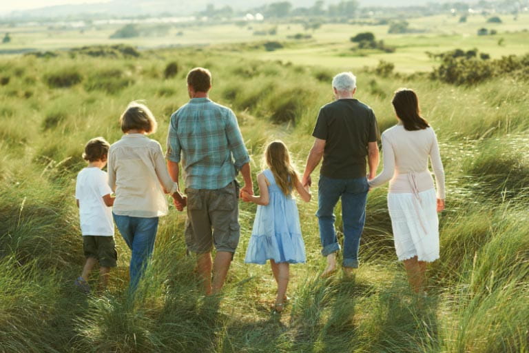 A family group of 6 people holding hands walking through a field