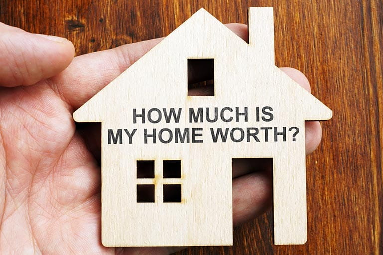 Wooden cut-out of a house with text that reads 'how much is my home worth?'