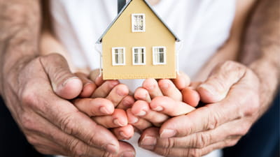 An adult and child's hands cupped together holding a small wooden house