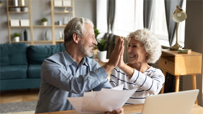 A mature couple high-fiving while looking at paperwork in their kitchen