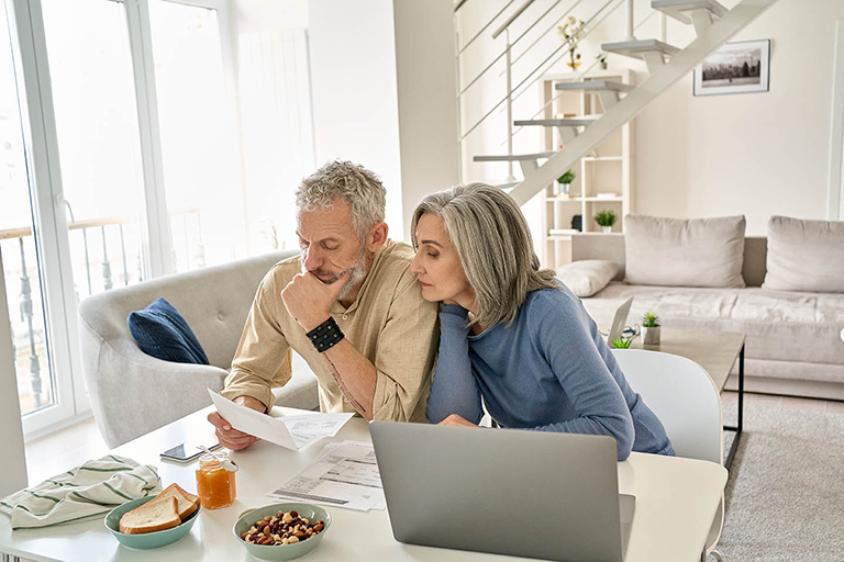 Two people sitting in a kitchen with a laptop looking at a document