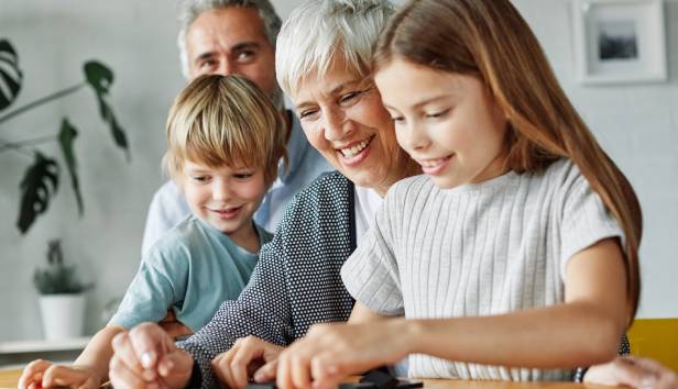 Grandparents sitting with their grandchildren smiling playing board games together