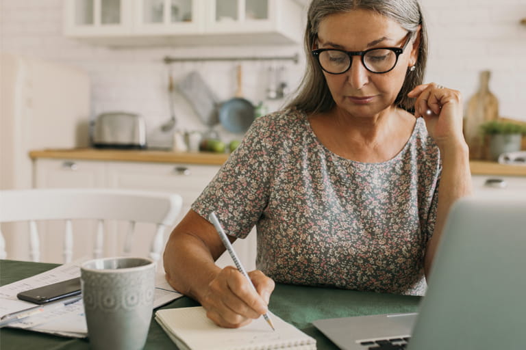 Person wearing glasses at a laptop making notes