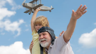 A grandfather carrying his grandson in the air as they play with a toy airplane