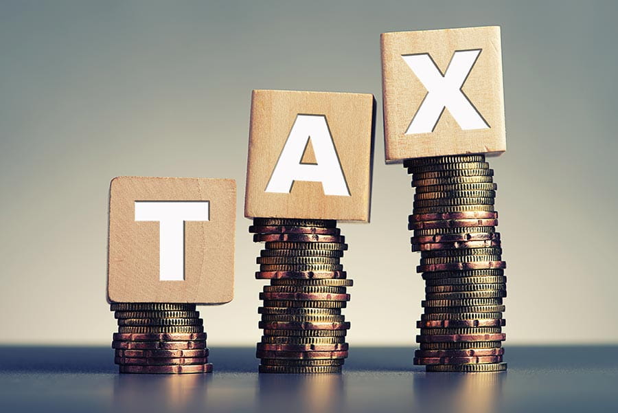3 piles of coins with wooden blocks spelling out tax