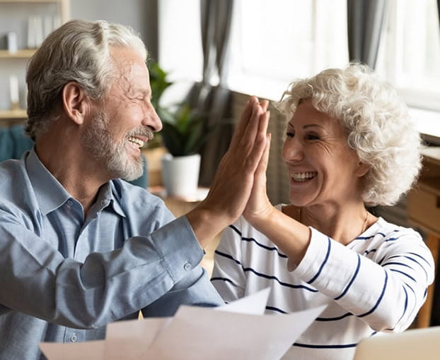 A mature couple high-fiving while looking at paperwork in their kitchen