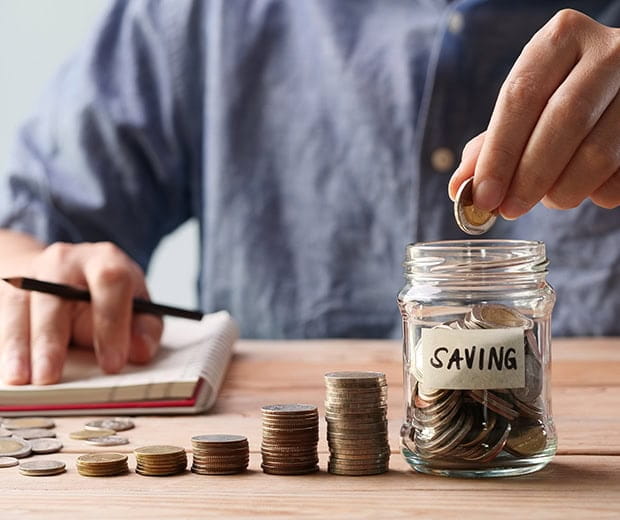 A table with piles of coins in increasing heights with a glass jar full of coins next to them with a label saying savings