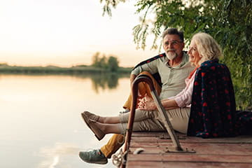 Mature couple relaxing on a pier, sharing a blanket and enjoying the sunset over the lake.