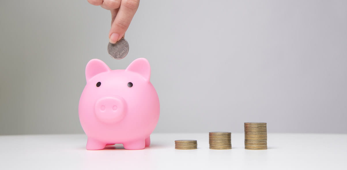 A piggy bank with piles of coins next to it in increasing size