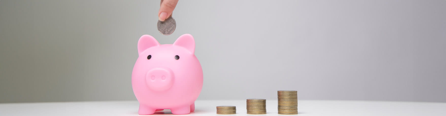 A piggy bank with piles of coins next to it in increasing size