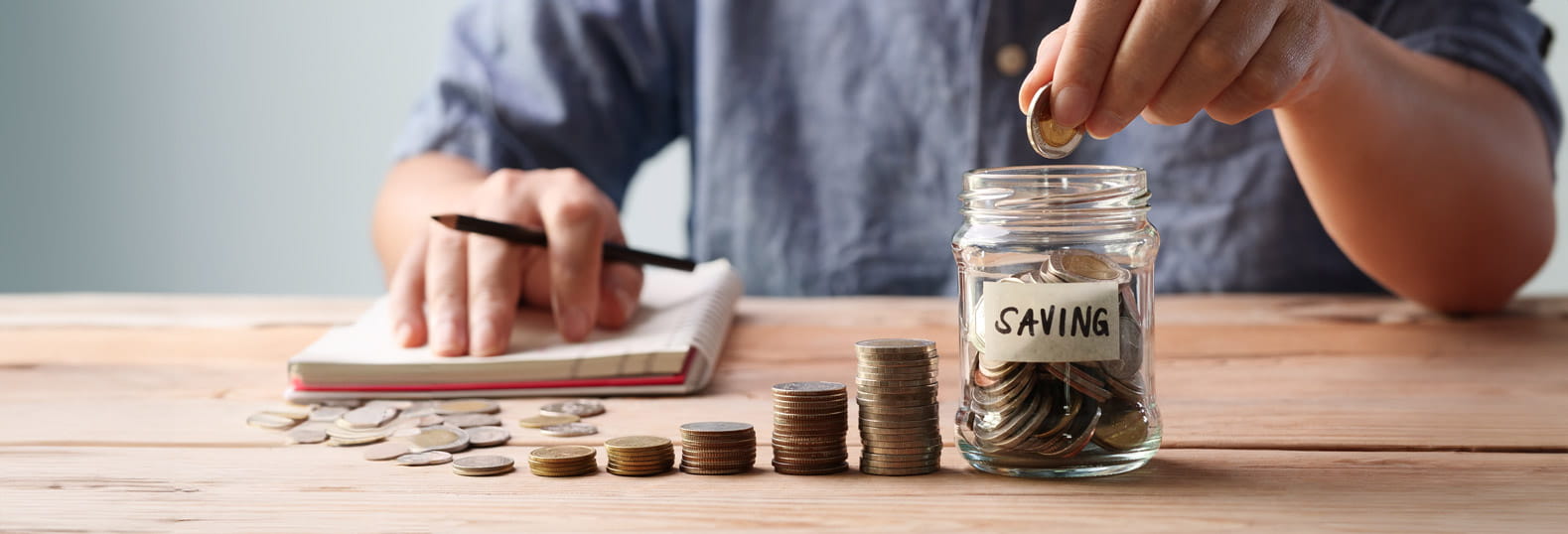 A table with piles of coins in increasing heights with a glass jar full of coins next to them with a label saying savings