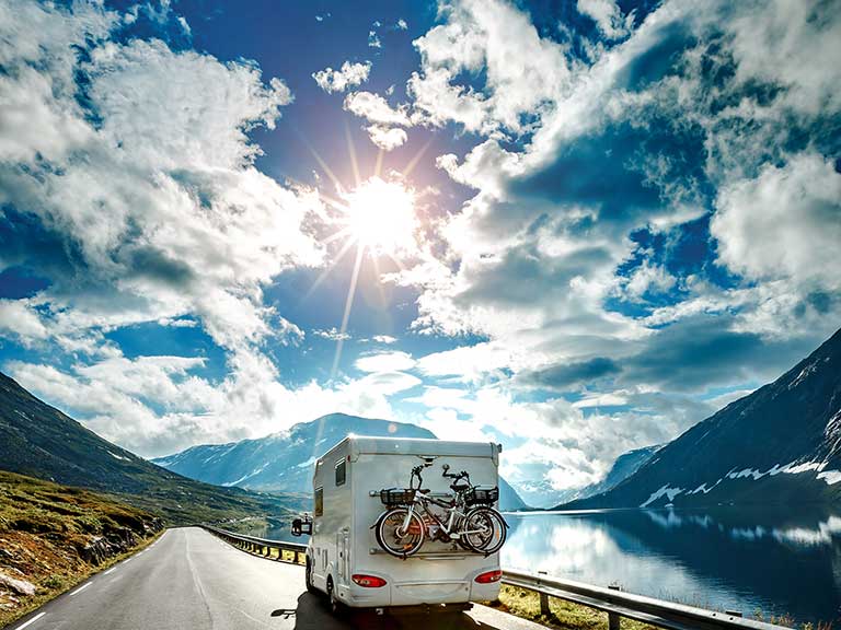 A caravan drives past a lake towards the sun