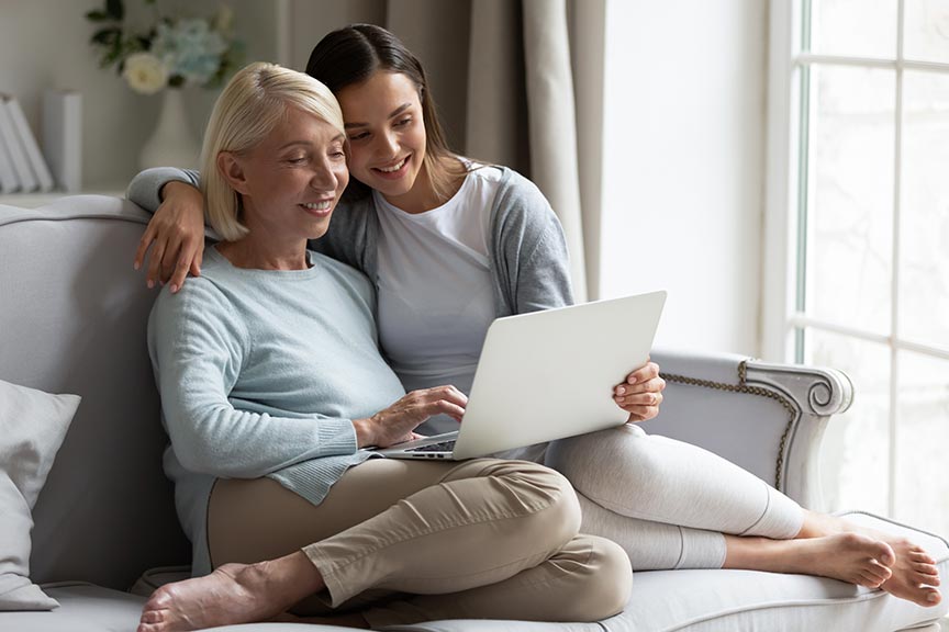 A mother and daughter sitting on the sofa looking at a laptop