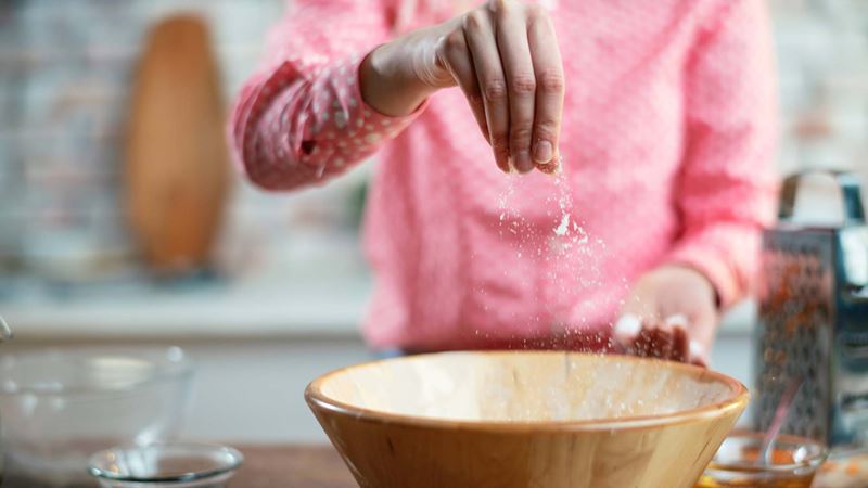 A woman in a pink jumper adding salt into a mixing bowl